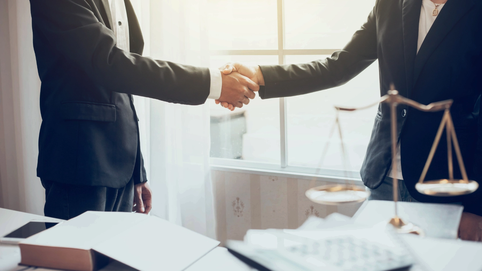 Zwei Männer schütteln sich die Hand neben einer Richterwaage auf dem Tisch, dort sind auch Akten zu sehen